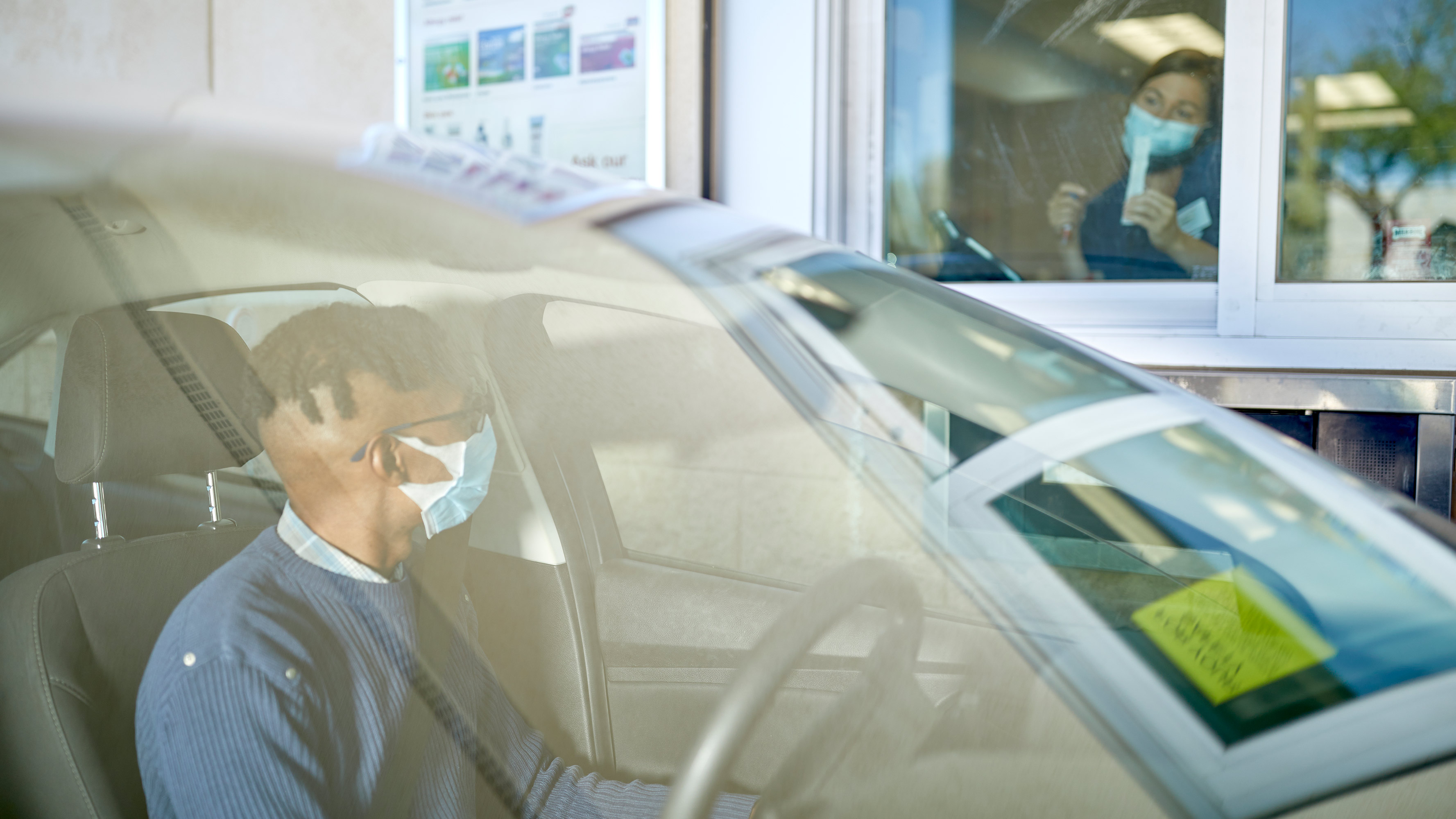 Megan Chesnet coaches a patient, from behind the window at a CVS Pharmacy drive-thru location, about how to administer a COVID-19 nasal swab test.