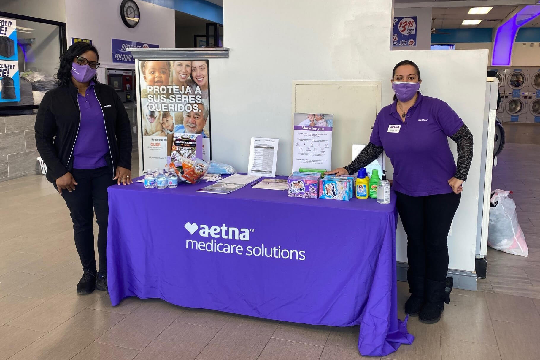 Two masked Aetna representatives provide free laundry products from a table stocked with products.