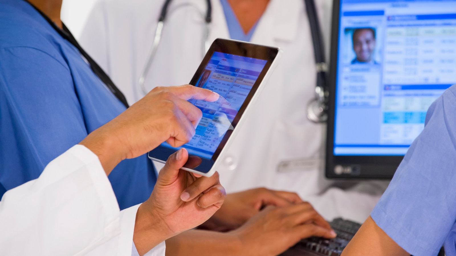 A group of healthcare providers use a tablet and a computer to look up patient data.